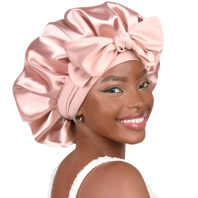Woman smiling and wearing a pink satin bonnet with a large bow, styled for hair protection.