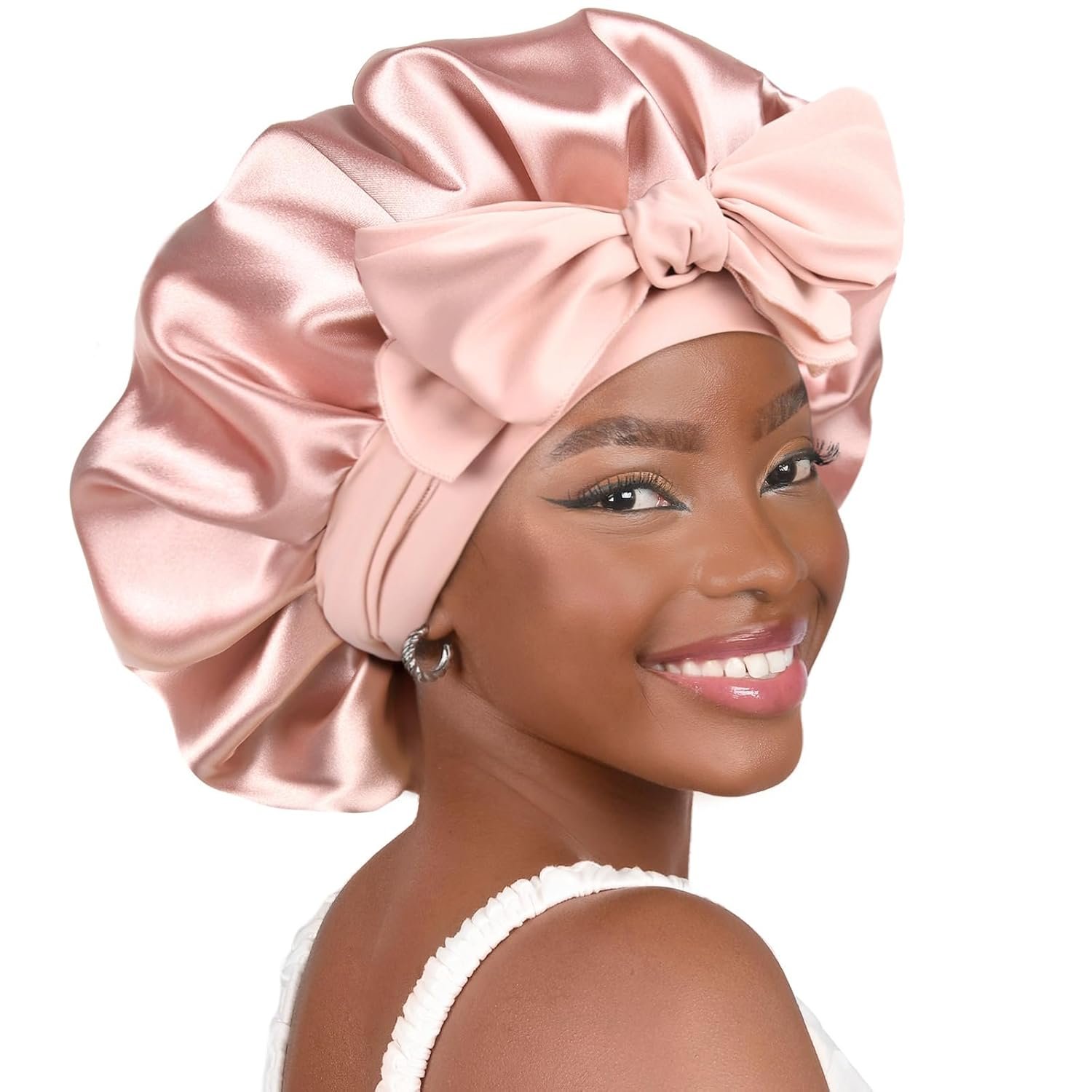 Woman smiling and wearing a pink satin bonnet with a large bow, styled for hair protection.