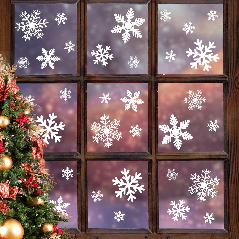 Christmas snowflake window stickers on glass panes with a decorated Christmas tree beside them.