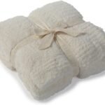 A cream-colored fluffy blanket neatly folded and tied with a beige ribbon labeled “BAREFOOT DREAMS.”